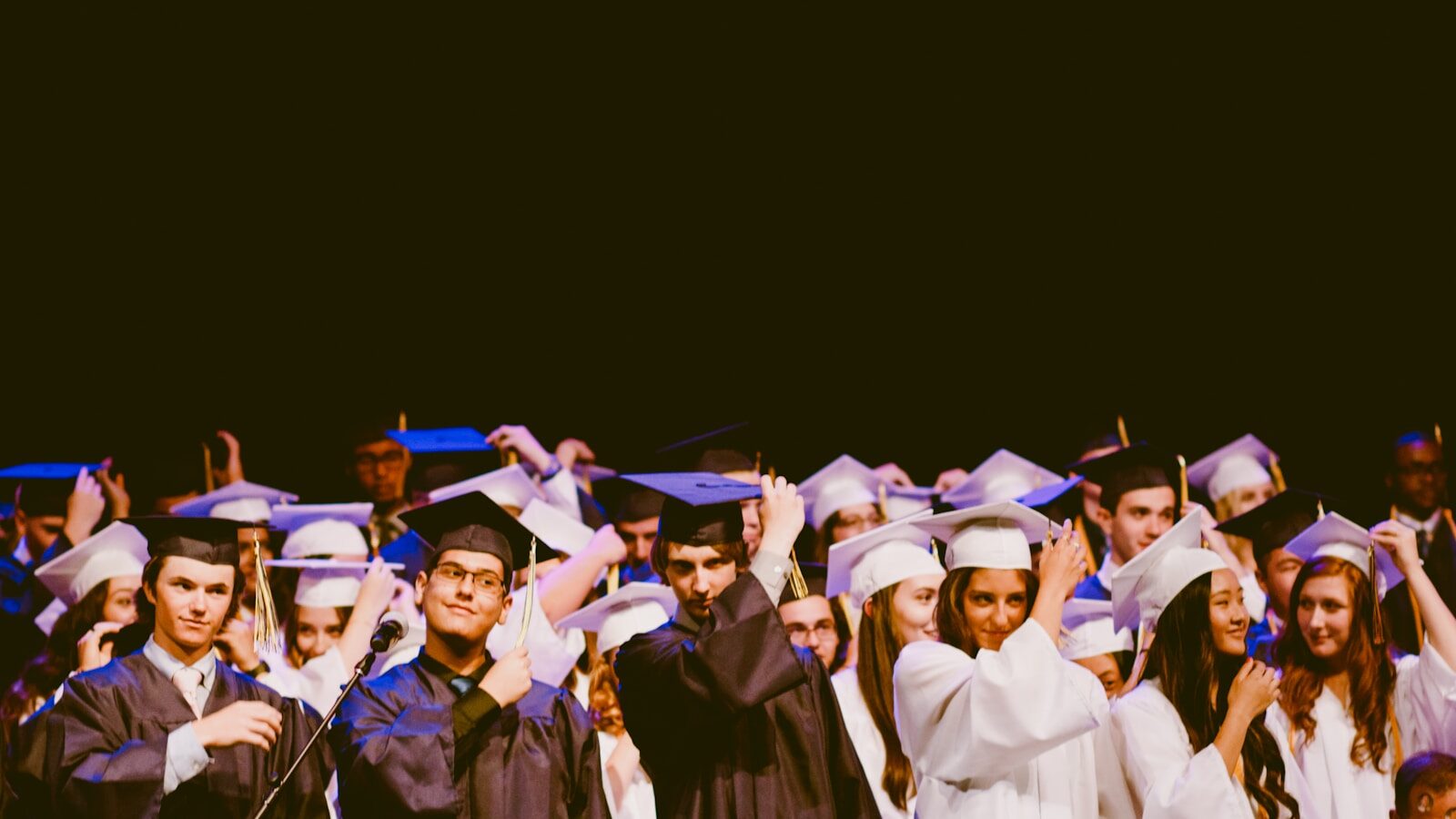 Men and women wearing black and white graduation gowns and mortar caps inside a building, illustrating the end goal of researching potential graduate programs.